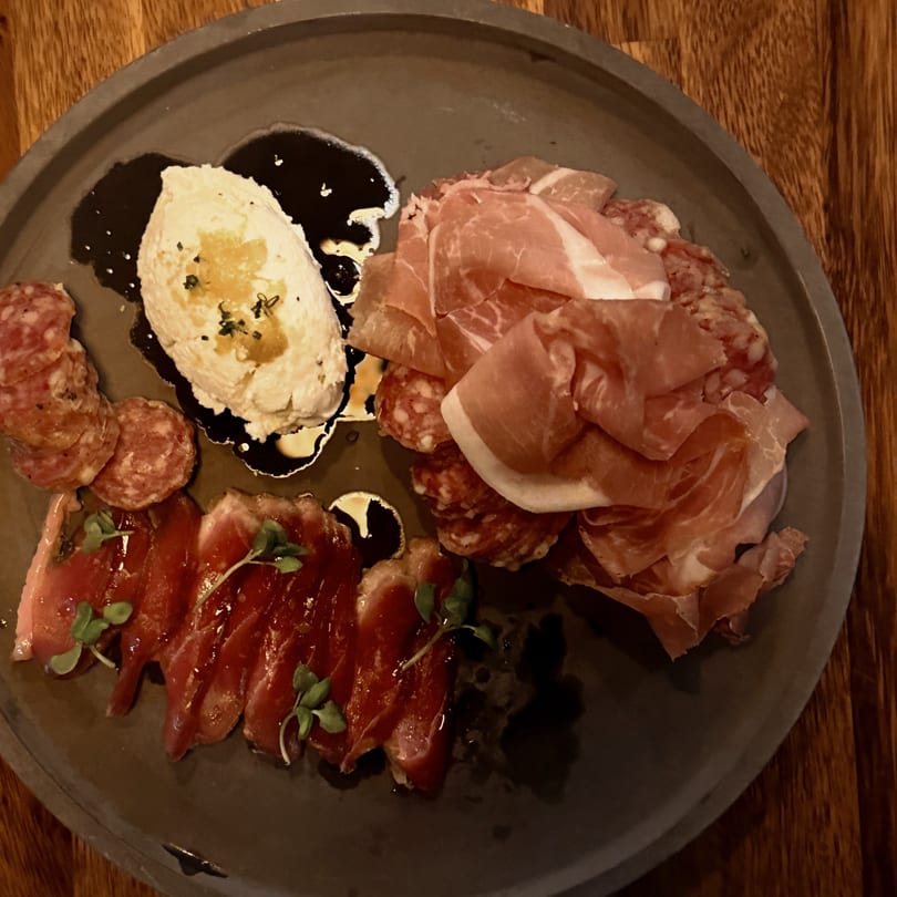 Charcuterie board with prosciutto, salami, sliced meat, ricotta cheese, and balsamic glaze.