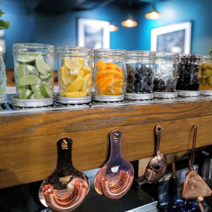 Mason jars filled with sliced limes, lemons, oranges, and blueberries on a bar top.