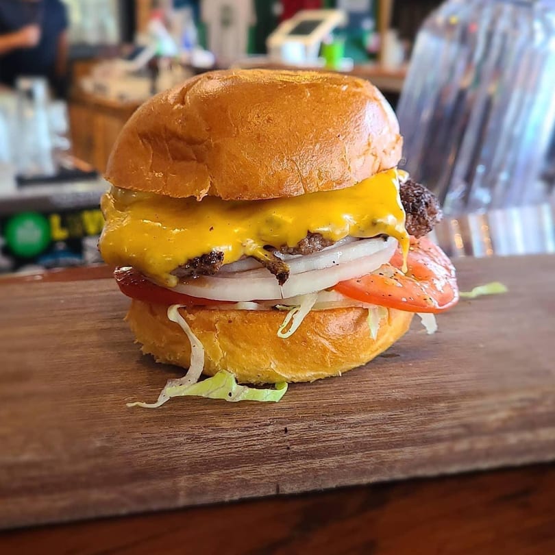 Cheeseburger with melted cheese, onions, tomato, and lettuce on a wooden board at Evergreen Brewery.
