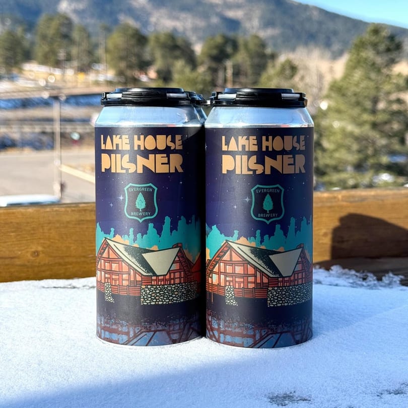 Two Evergreen Brewery Lake House Pilsner cans sit in snow with mountains in the background.